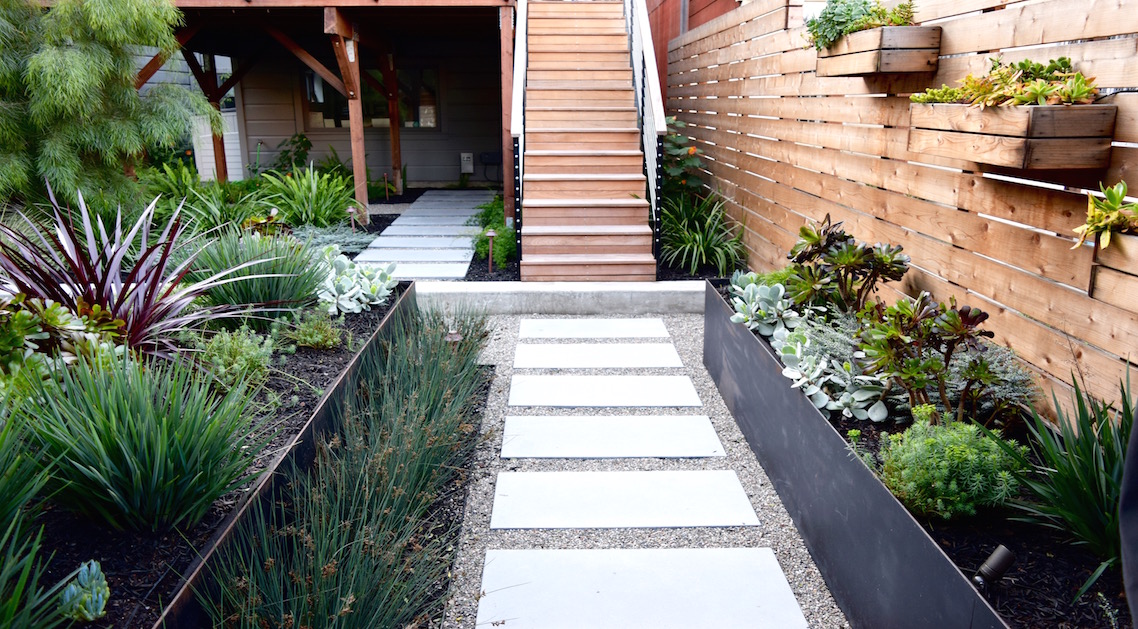 back yard with paved pathways, metal planters and wooden fence.