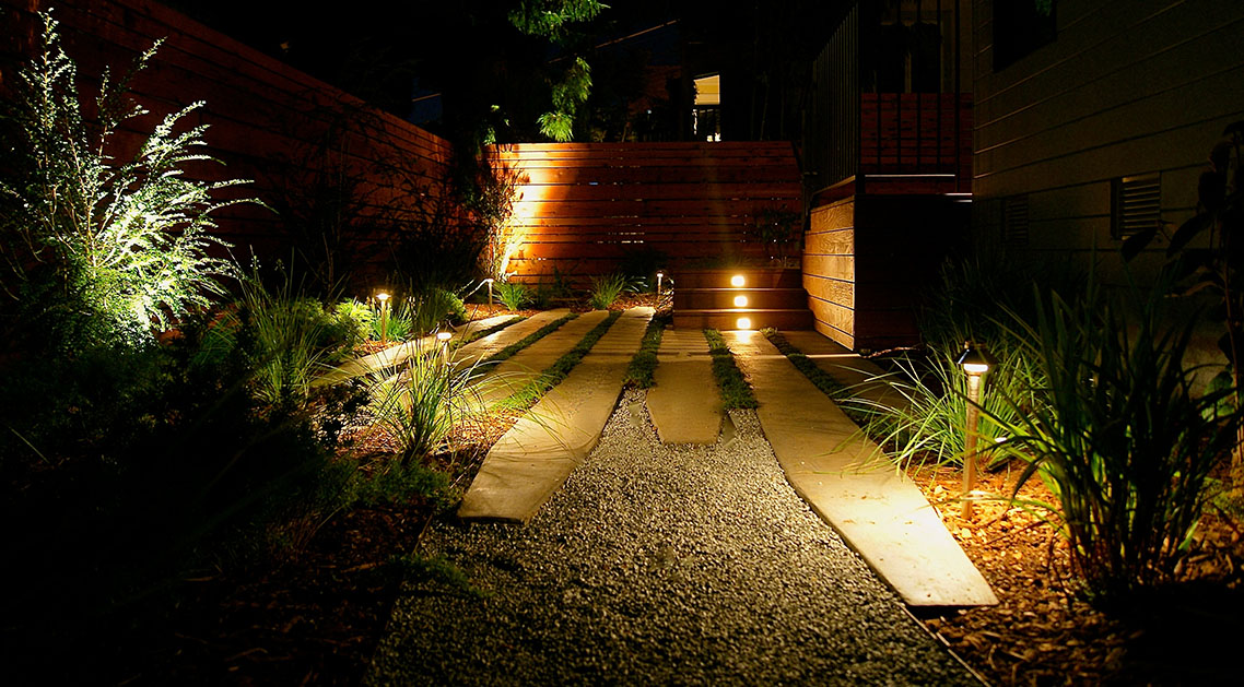 backyard at night with outdoor lamps, paved walkway and lit steps