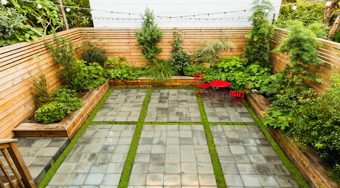 paved back yard enclosed by natural wood slat fence with built-in planters and variety of plants.