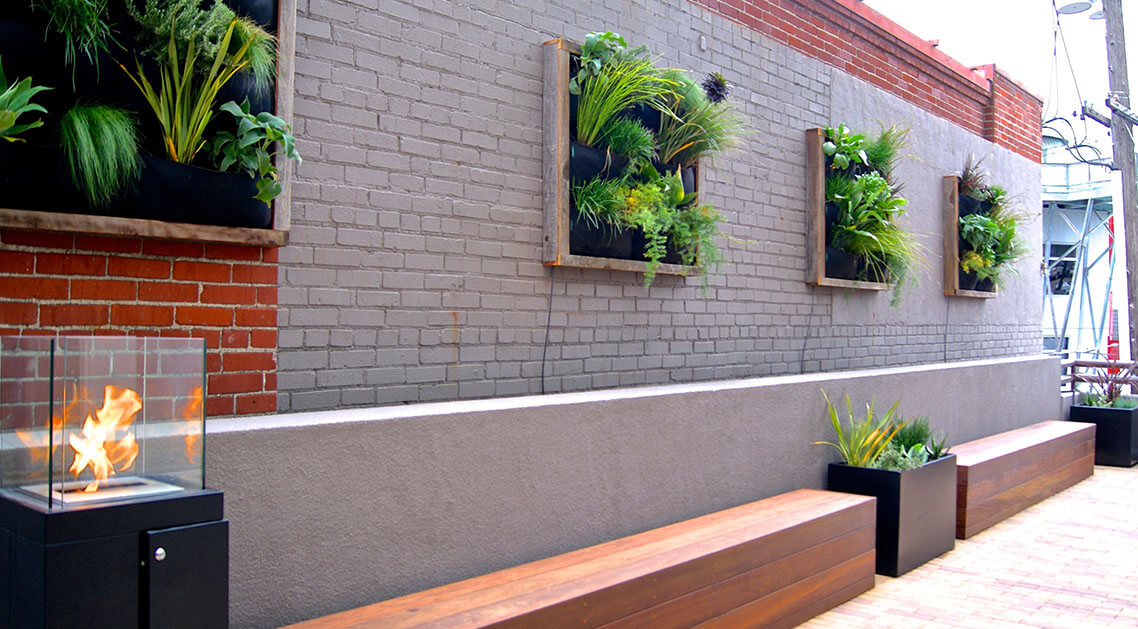 brick wall featuring four living plant wall installations above planters and benches.