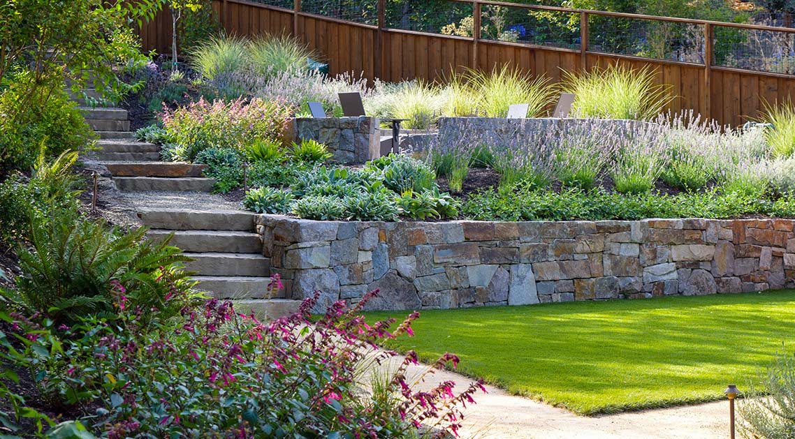 Tiered stone walled back yard with professional landscaping including terraces, lawn, pathways and lighting