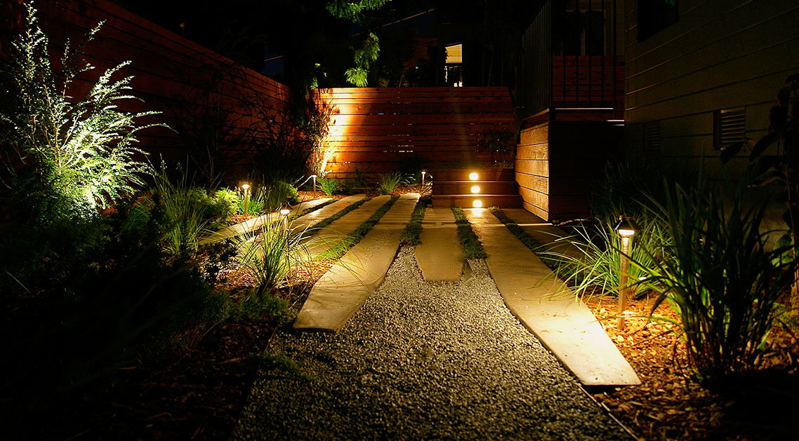backyard at night with outdoor lamps, paved walkway and lit steps